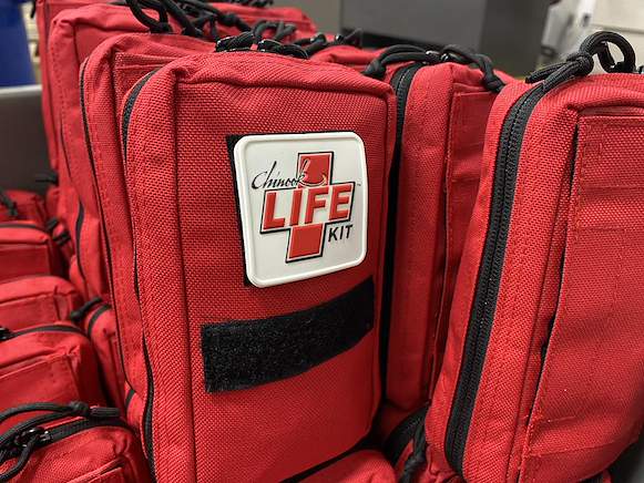 A row of red Chinook LIFE Kit bags with matching front labels.